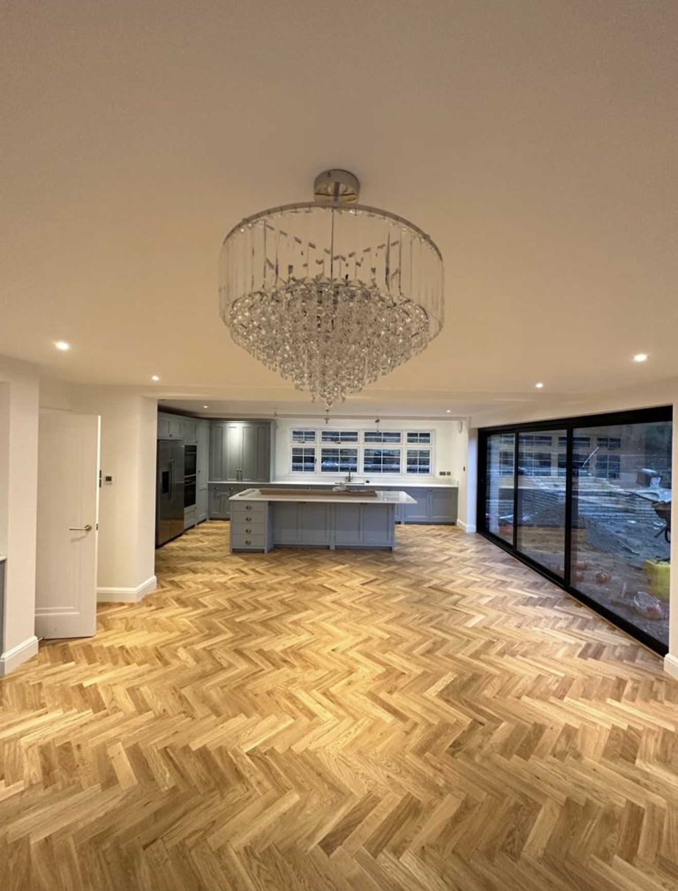 Finished open-plan kitchen with herringbone parquet flooring and statement chandelier